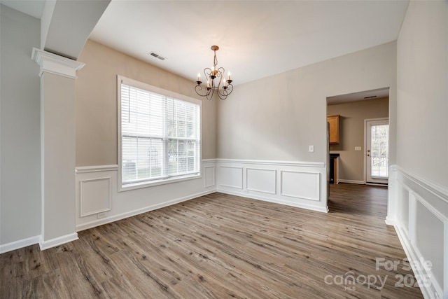 unfurnished room featuring an inviting chandelier, decorative columns, and light wood-type flooring