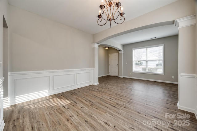 empty room with decorative columns, hardwood / wood-style floors, and a notable chandelier