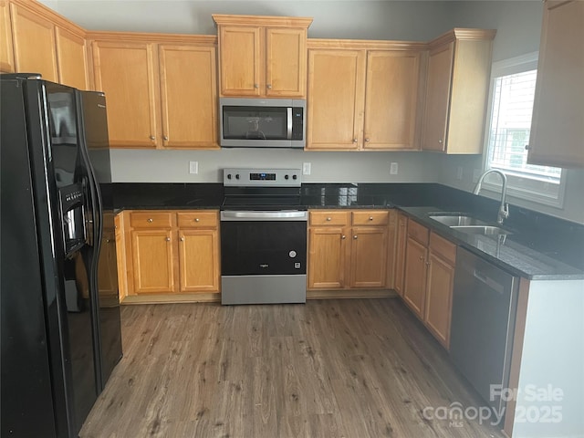 kitchen featuring appliances with stainless steel finishes, sink, hardwood / wood-style floors, and dark stone countertops