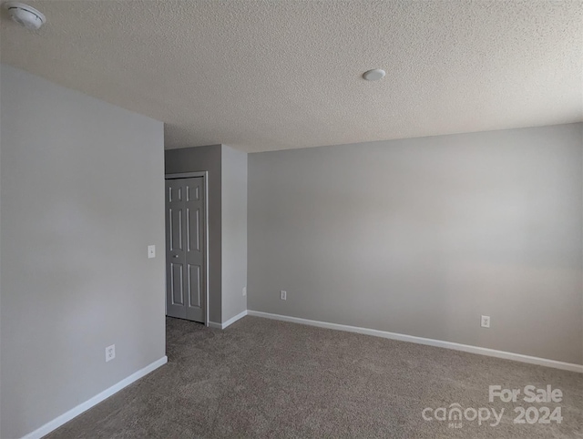 unfurnished room with a textured ceiling and dark carpet