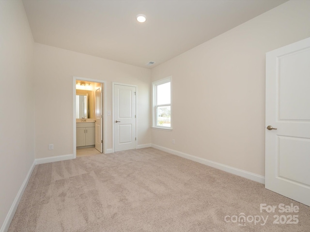 unfurnished bedroom with light colored carpet, baseboards, and ensuite bathroom