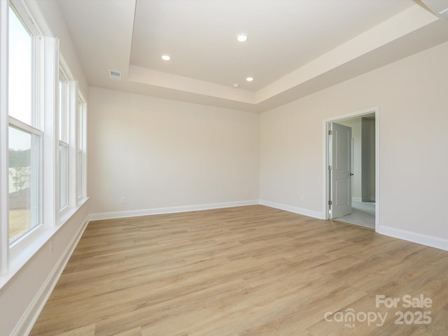 unfurnished room with light wood finished floors, visible vents, baseboards, and a tray ceiling