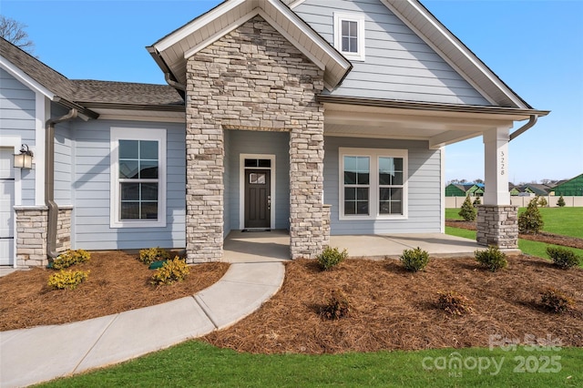 craftsman house featuring stone siding, covered porch, and roof with shingles