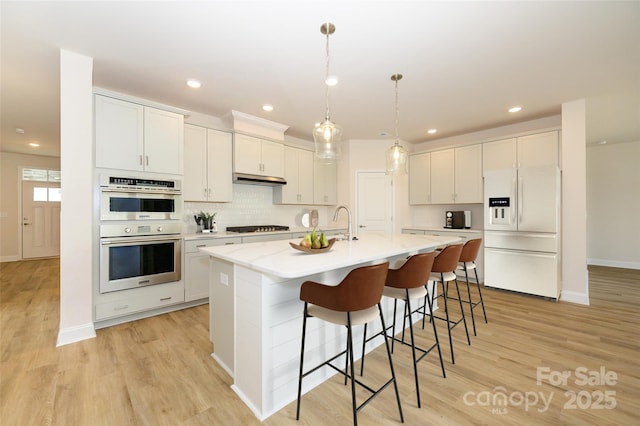 kitchen featuring tasteful backsplash, white fridge with ice dispenser, light wood-style flooring, stainless steel double oven, and gas stovetop