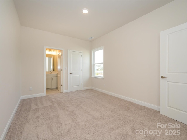 unfurnished bedroom featuring baseboards, connected bathroom, and light carpet
