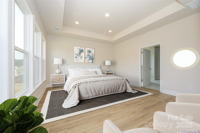 bedroom with baseboards, recessed lighting, visible vents, a tray ceiling, and wood finished floors