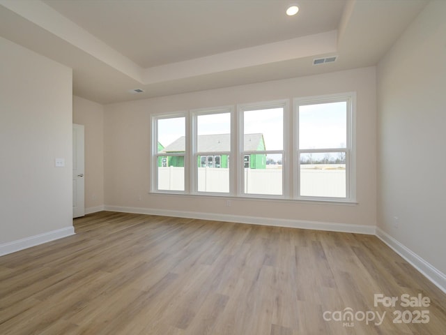 unfurnished room featuring visible vents, a tray ceiling, baseboards, and light wood-style flooring