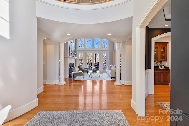 foyer entrance with light wood-type flooring, a towering ceiling, and ornate columns