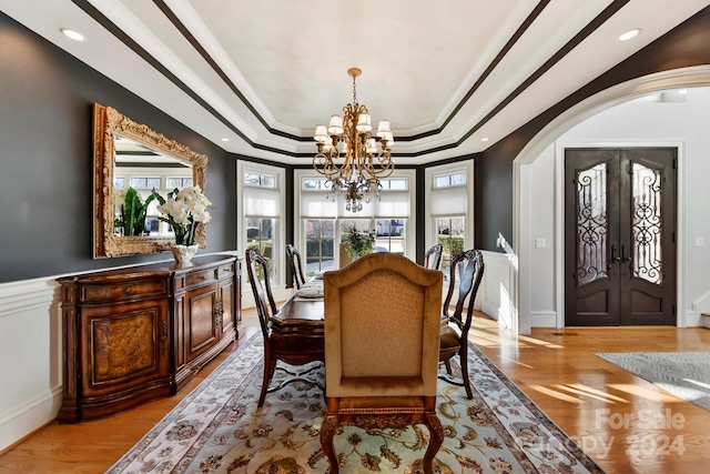 dining room with light hardwood / wood-style floors, a tray ceiling, french doors, ornamental molding, and a chandelier