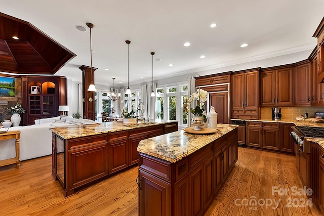 kitchen with an island with sink, light stone countertops, light hardwood / wood-style flooring, decorative light fixtures, and sink