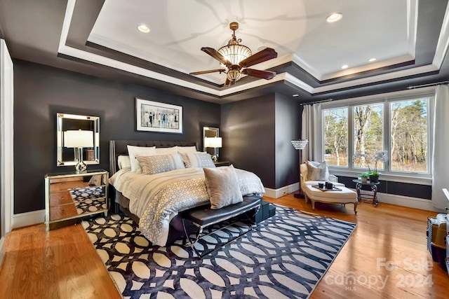 bedroom with wood-type flooring, a raised ceiling, crown molding, and ceiling fan