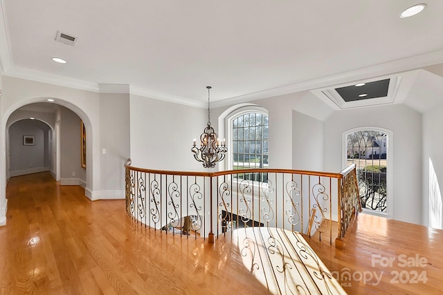 hallway with an inviting chandelier, light hardwood / wood-style floors, plenty of natural light, and ornamental molding