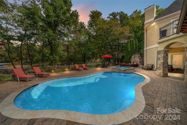 pool at dusk with an in ground hot tub and a patio area