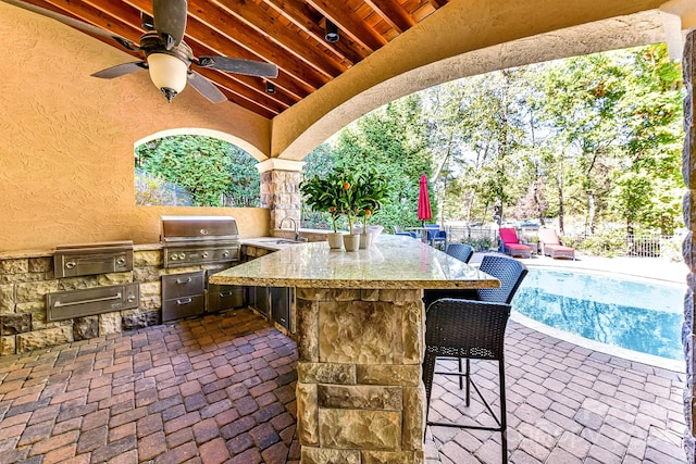 view of patio featuring ceiling fan, grilling area, an outdoor kitchen, and a wet bar