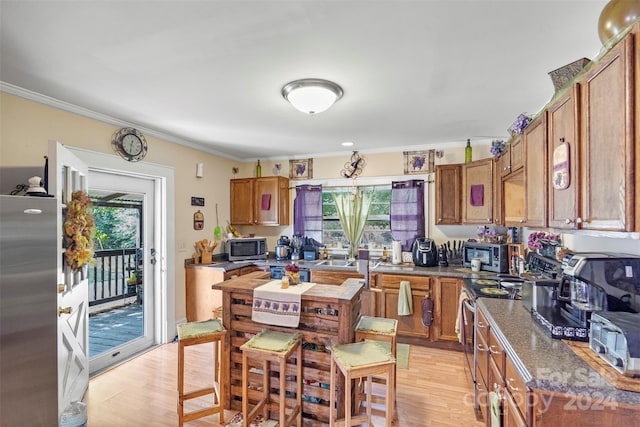 kitchen with dark stone countertops, ornamental molding, light hardwood / wood-style flooring, and stainless steel appliances