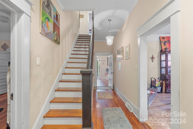 staircase with a healthy amount of sunlight, crown molding, and hardwood / wood-style floors