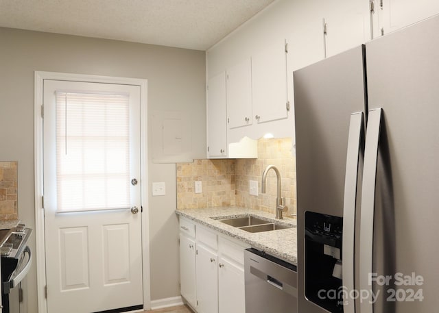 kitchen featuring sink, white cabinets, backsplash, appliances with stainless steel finishes, and light stone countertops