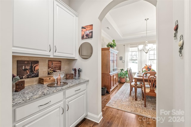 bar featuring light stone counters, dark hardwood / wood-style floors, white cabinets, a tray ceiling, and hanging light fixtures