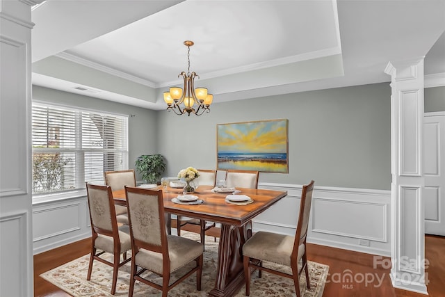 dining room featuring dark wood-type flooring, a raised ceiling, a notable chandelier, decorative columns, and ornamental molding