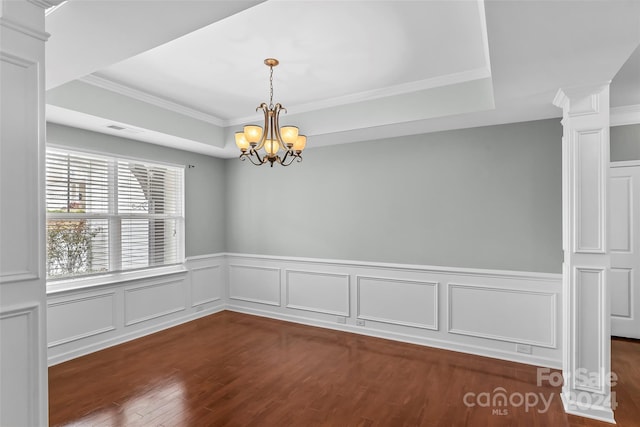 spare room with an inviting chandelier, dark hardwood / wood-style floors, decorative columns, crown molding, and a tray ceiling