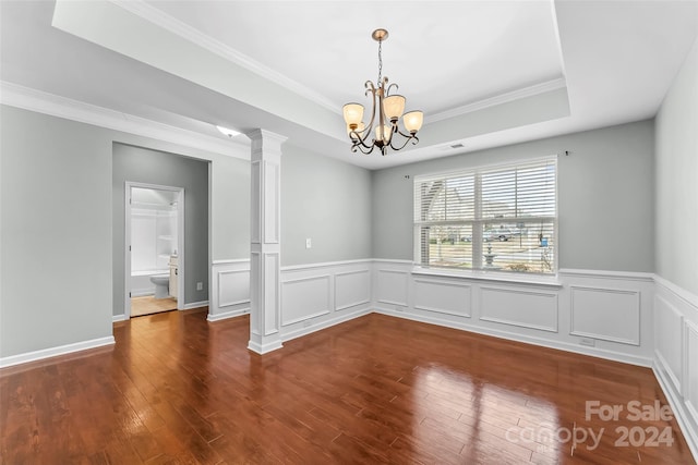 spare room with dark hardwood / wood-style flooring, ornate columns, ornamental molding, a tray ceiling, and a chandelier