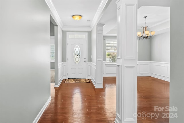 foyer with dark hardwood / wood-style floors, an inviting chandelier, crown molding, and ornate columns