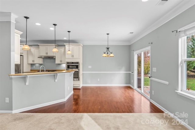 kitchen with pendant lighting, sink, crown molding, double oven, and a kitchen bar