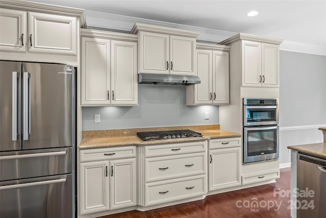 kitchen featuring stainless steel appliances, light stone counters, dark hardwood / wood-style flooring, crown molding, and cream cabinetry