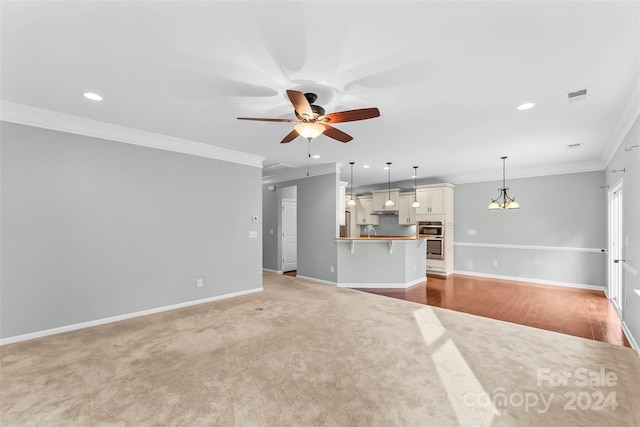 unfurnished living room featuring carpet, ceiling fan with notable chandelier, and crown molding