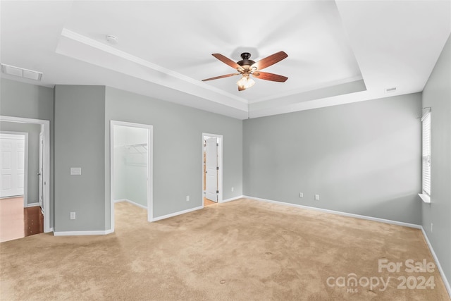 unfurnished bedroom featuring ceiling fan, a raised ceiling, a walk in closet, and a closet