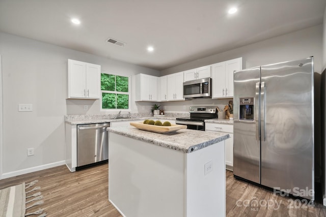 kitchen with white cabinets, appliances with stainless steel finishes, light hardwood / wood-style floors, and a center island