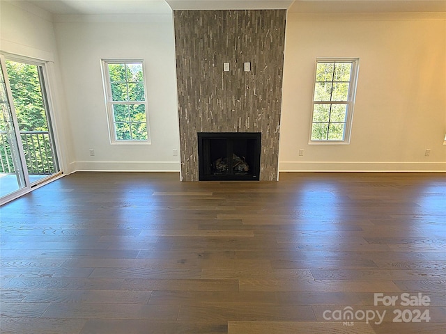 unfurnished living room featuring crown molding, dark wood-type flooring, a fireplace, and a wealth of natural light