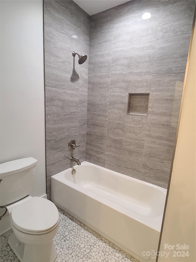 bathroom with toilet, tiled shower / bath combo, and tile patterned flooring