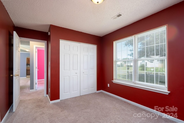 unfurnished bedroom with light carpet, a textured ceiling, and a closet