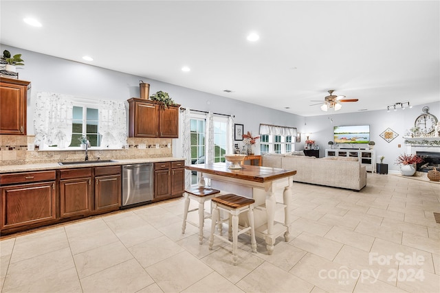 kitchen featuring a kitchen breakfast bar, decorative backsplash, ceiling fan, stainless steel dishwasher, and sink