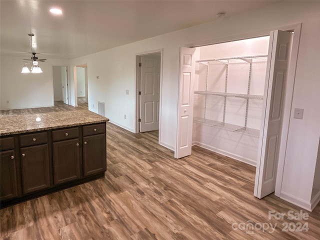 kitchen featuring dark brown cabinets, ceiling fan, wood-type flooring, and light stone countertops