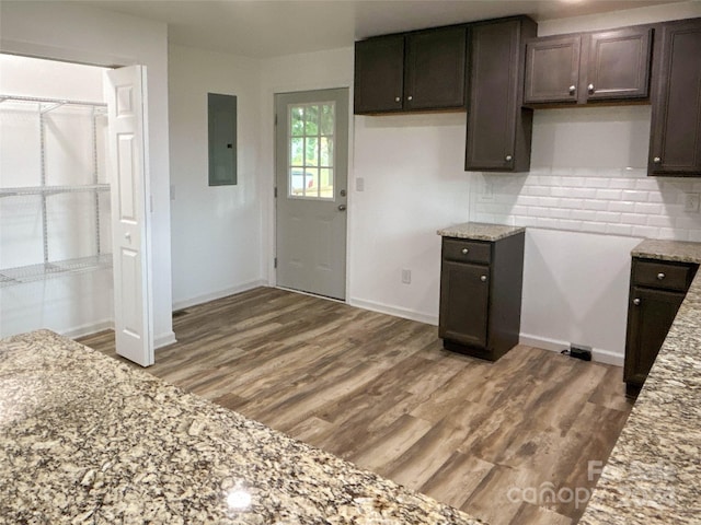 kitchen featuring electric panel, hardwood / wood-style flooring, decorative backsplash, light stone countertops, and dark brown cabinetry