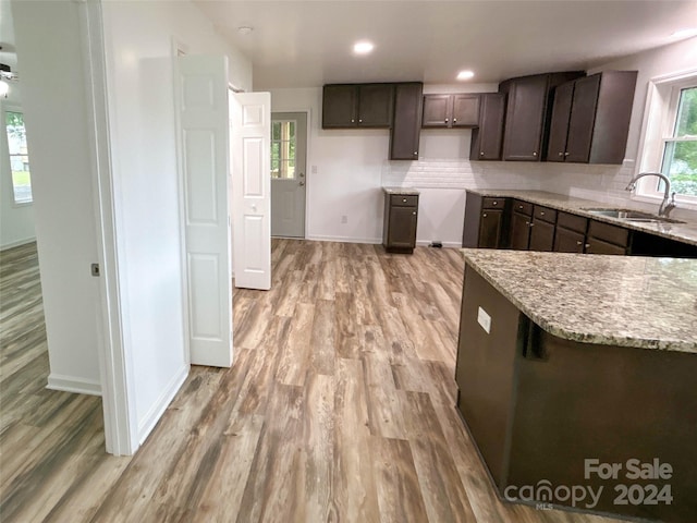 kitchen with dark brown cabinetry, light stone countertops, sink, tasteful backsplash, and light hardwood / wood-style floors