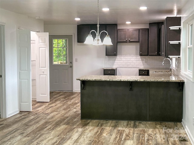 kitchen with kitchen peninsula, wood-type flooring, light stone countertops, and hanging light fixtures