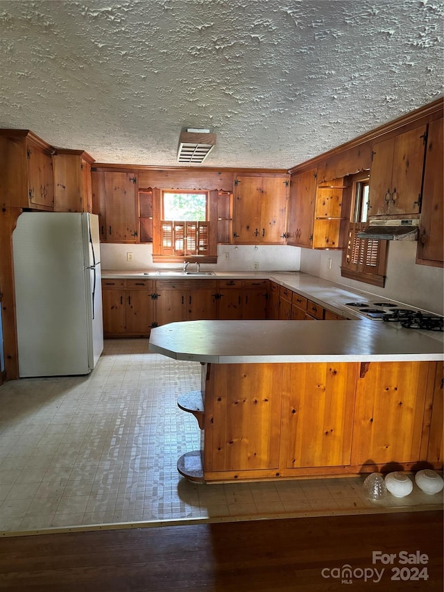 kitchen featuring light wood-type flooring, white refrigerator, a textured ceiling, kitchen peninsula, and extractor fan