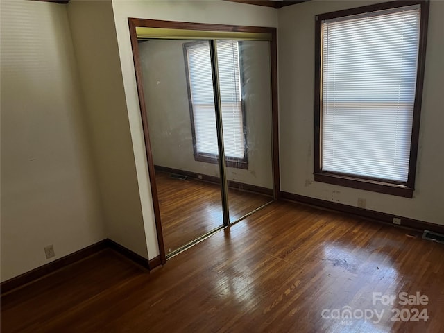 unfurnished bedroom featuring multiple windows, dark hardwood / wood-style floors, and a closet