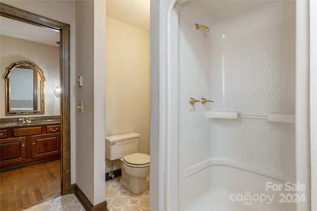 bathroom featuring wood-type flooring, vanity, toilet, and walk in shower