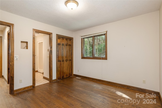 unfurnished bedroom with a textured ceiling, dark wood-type flooring, and a closet