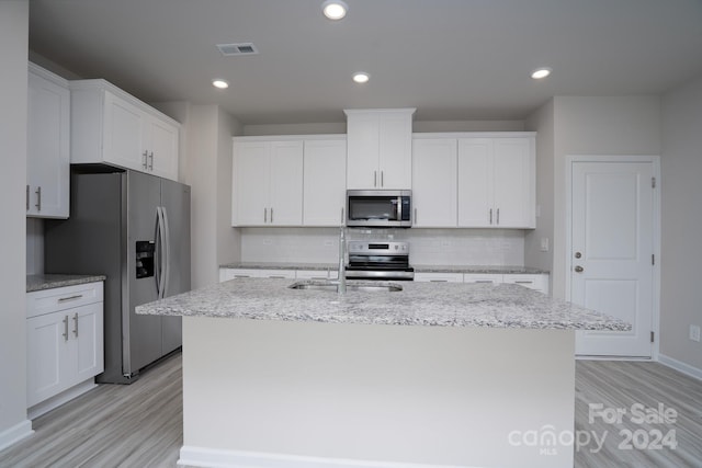 kitchen with an island with sink, stainless steel appliances, white cabinets, and decorative backsplash