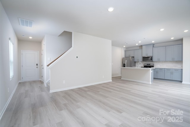 kitchen with sink, stainless steel appliances, tasteful backsplash, an island with sink, and light wood-type flooring