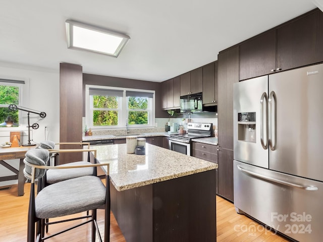 kitchen featuring a kitchen island, light stone countertops, light hardwood / wood-style floors, dark brown cabinetry, and stainless steel appliances