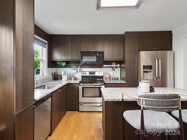 kitchen with dark brown cabinets, sink, light wood-type flooring, appliances with stainless steel finishes, and light stone counters