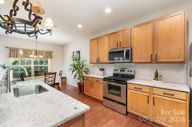 kitchen with hardwood / wood-style floors, a notable chandelier, sink, stainless steel appliances, and hanging light fixtures