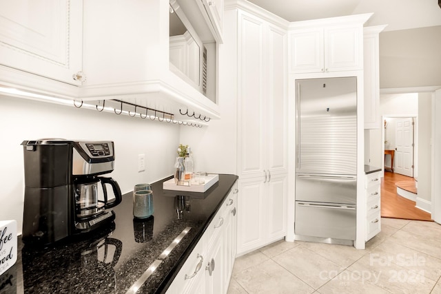 kitchen featuring dark stone counters, white cabinetry, light tile patterned floors, and high end fridge