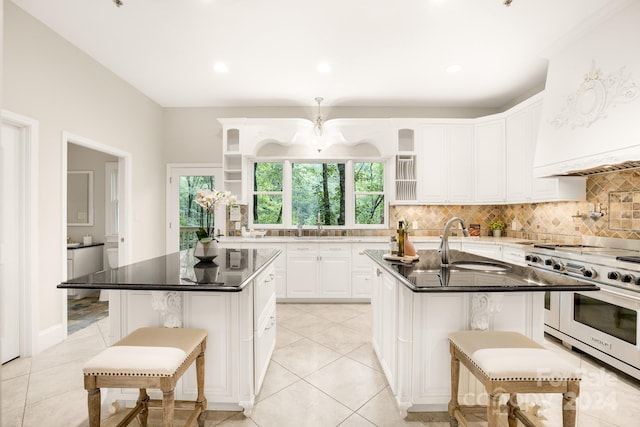 kitchen featuring a center island with sink, a kitchen bar, white cabinets, and range with two ovens